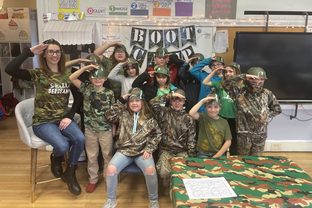 A classroom of elementary students wearing camouflage salute as they pose for a picture