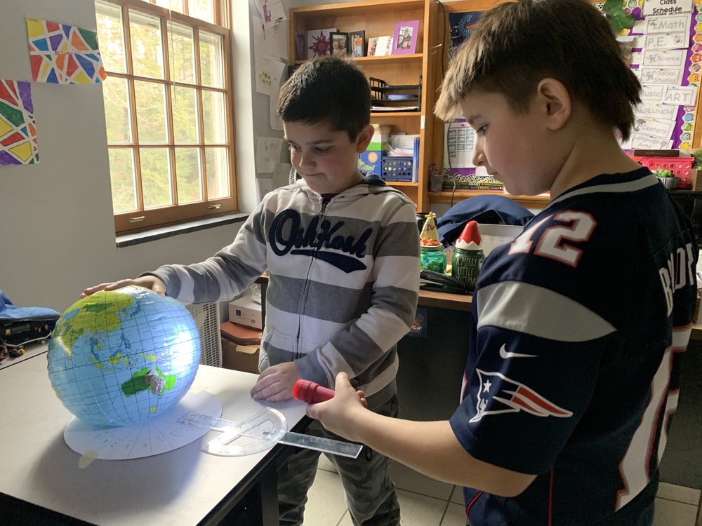 two young male students use a flashlight and a blow up earth model for a science experiment