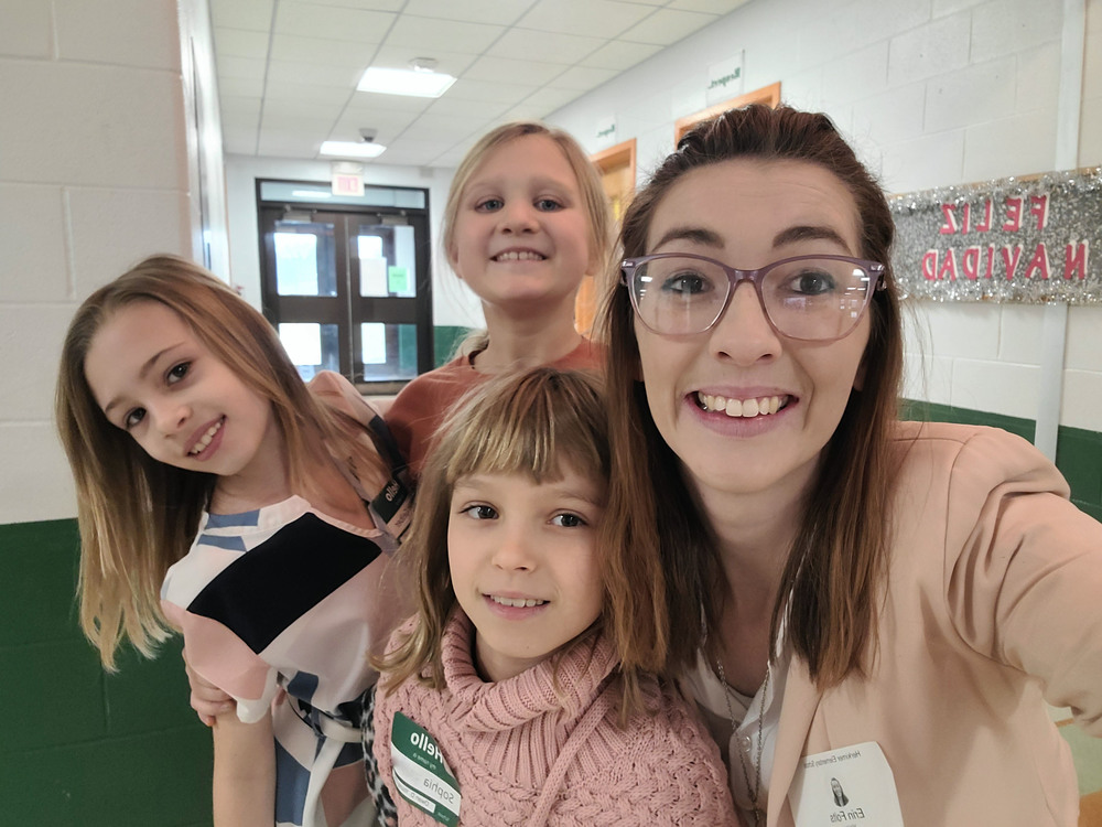 an adult woman wearing glasses poses with three of her young female students 