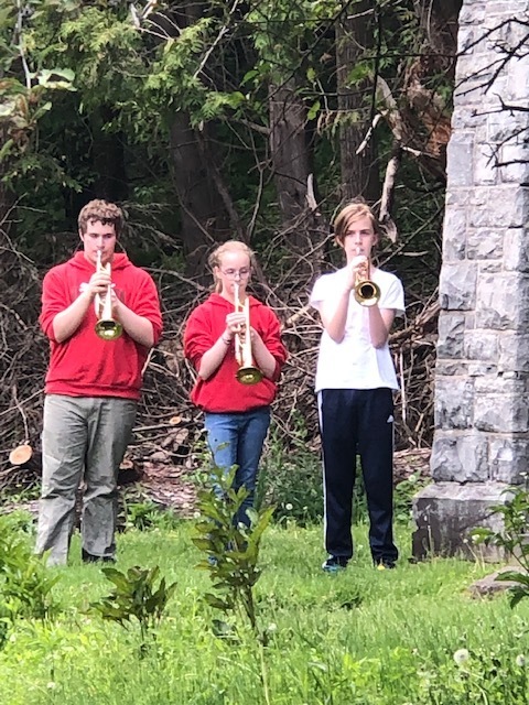three students play the trumpet outside in a cemetery